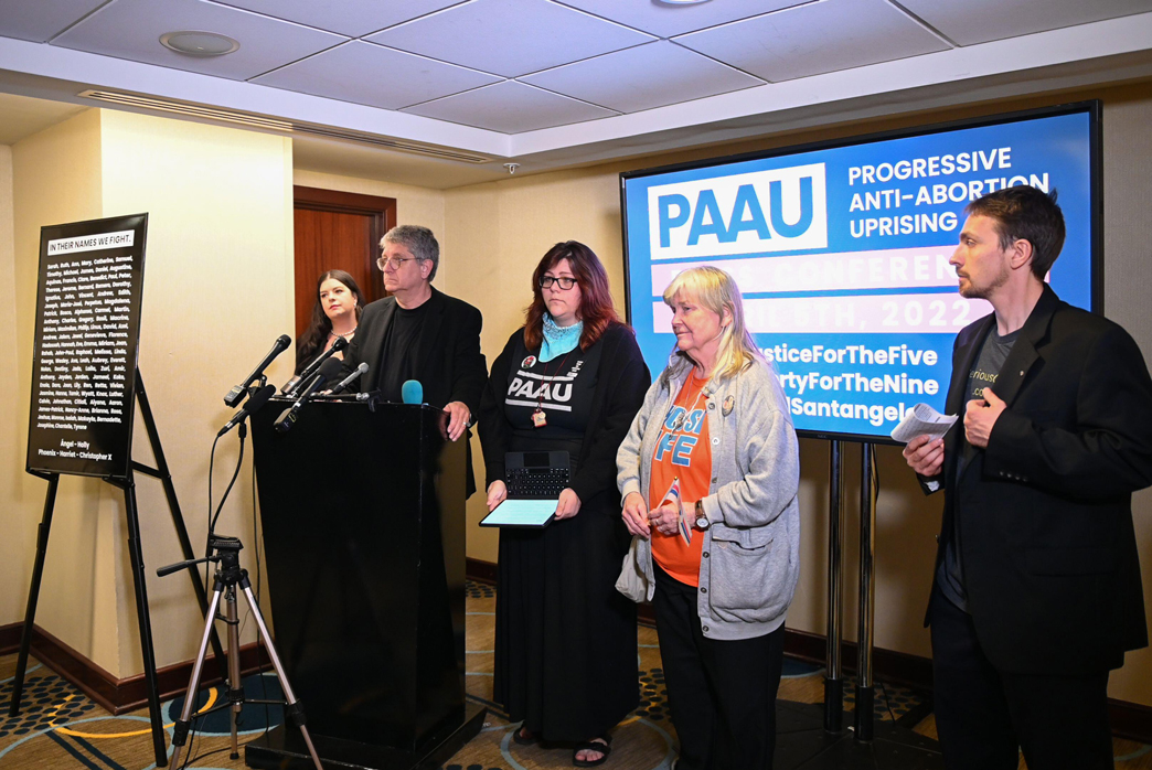 four people stand at a podium, in front of a sign that says 'Progressive Anti-Abortion Uprising'