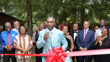 a man gives a speech next to a giant ribbon. people applaud