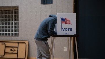 Person leans behind cardboard box labeled Vote to cast a ballot.