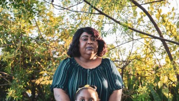 Portrait of woman outdoors hugging small girl who can only be seen from the eyes up.