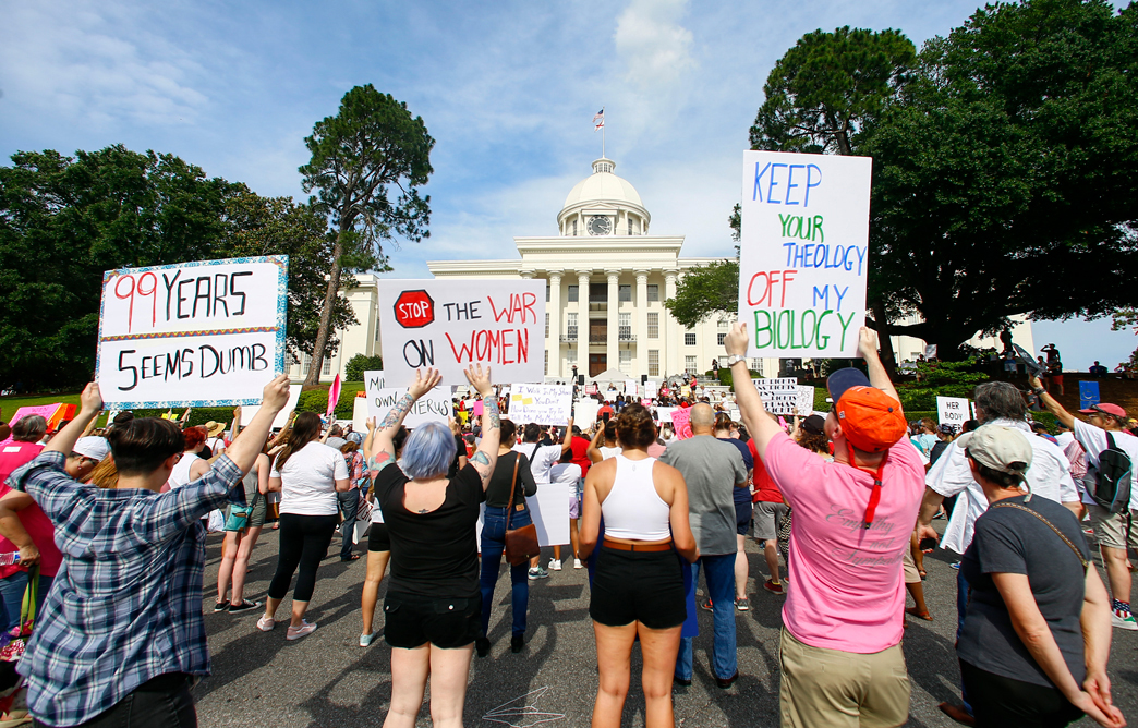 Protesters hold up signs in front of Alabama Capitol building.