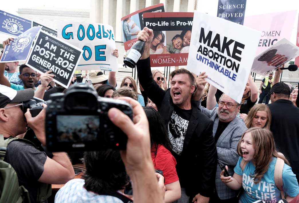 Camera in foreground captures a joyful group of people holding signs opposing abortion.