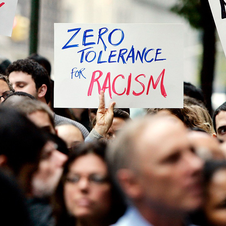 Person holds up sign during rally that reads "Zero Tolerance for Racism."