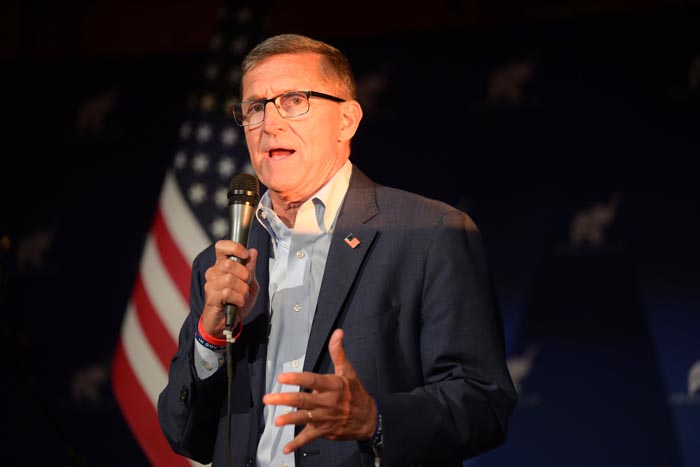 Michael Flynn, dressed in a suit, holds a microphone.