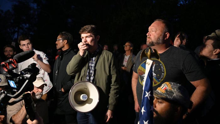 Nick Fuentes speaks into a megaphone with Alex Jones at his side.