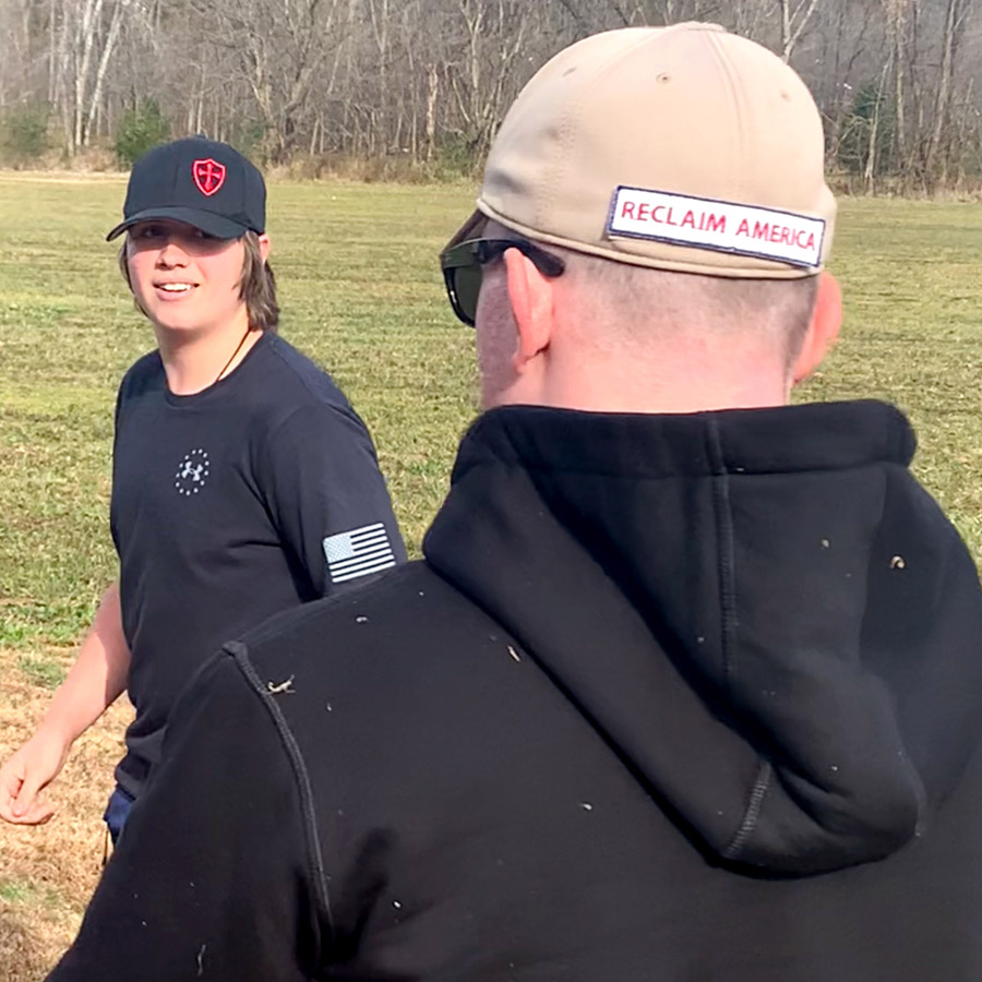 A person faces camera walking through a field looking at an individual whose back is facing the camera.